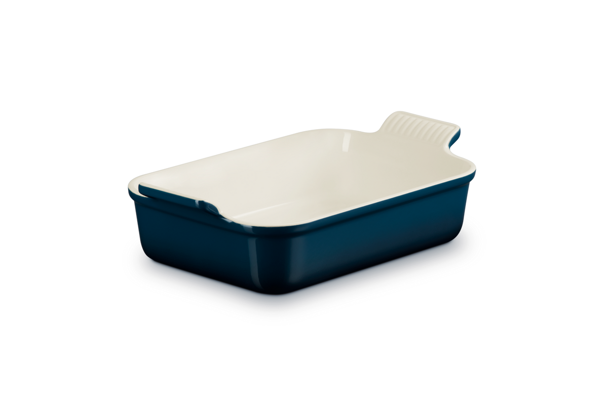 Le Creuset rectangular deep dish in Nuit blue with cream interior, shown at an angle on black background.