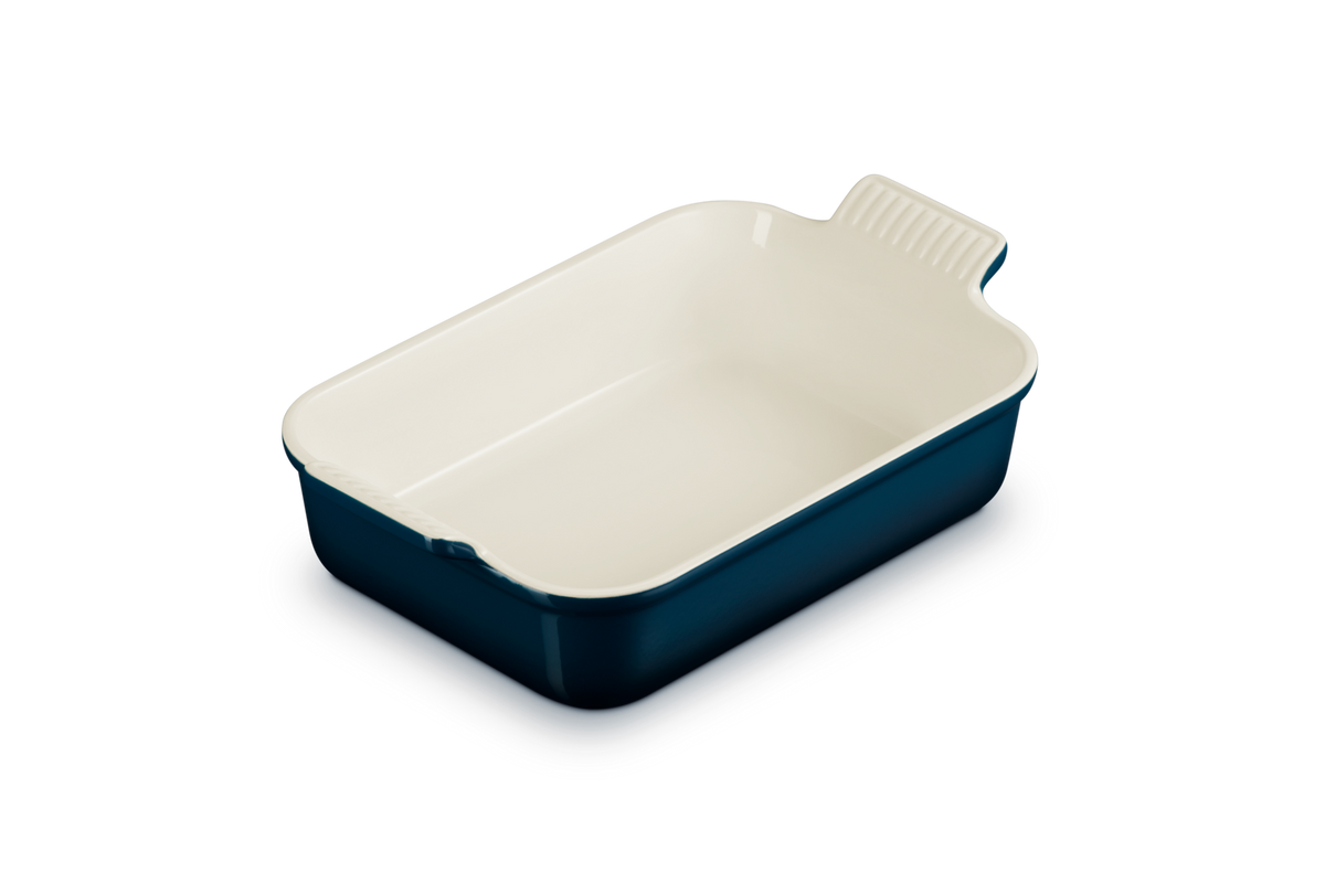 Le Creuset rectangular deep dish in dark blue with cream interior, shown at a slight angle.
