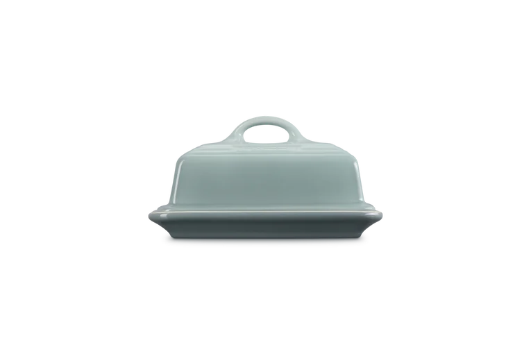 Le Creuset Stoneware Butter Dish in Sea Salt color, shown from the front on a black background.