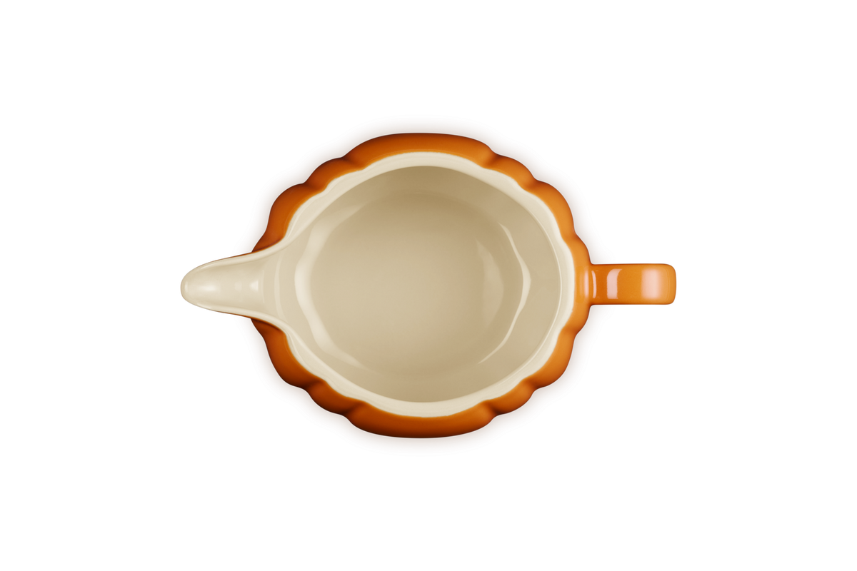 Top view of Le Creuset Halloween Pumpkin gravy boat in volcanic orange with cream interior and handle on the right.