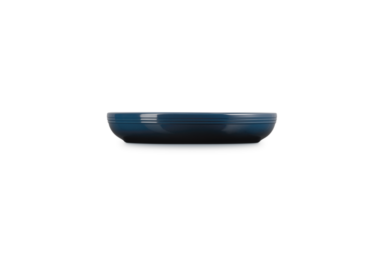 Le Creuset Coupe Pasta Bowl in deep blue, shown from a side profile on a black background.