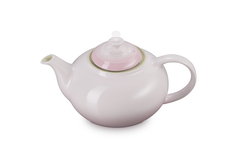 Le Creuset stoneware teapot in shell pink with rounded body, curved spout, and lid with infuser knob.