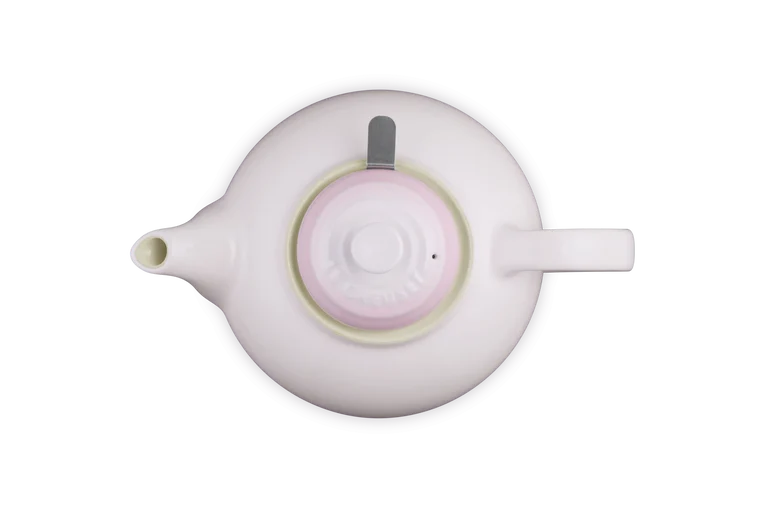 Top view of a shell pink Le Creuset stoneware teapot with lid and infuser handle visible on the right side.