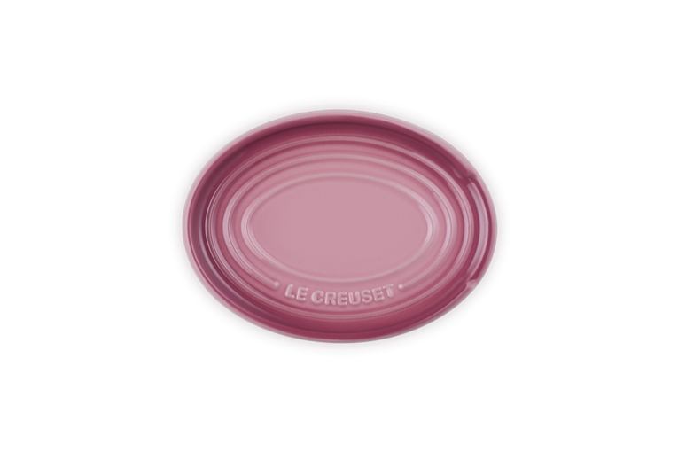 Le Creuset oval spoon rest in rose quartz with embossed logo and concentric ridges.