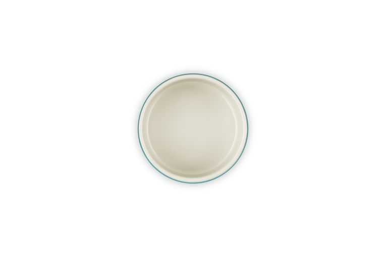 Top view of a blue Le Creuset stackable ramekin with a cream interior on a white background.