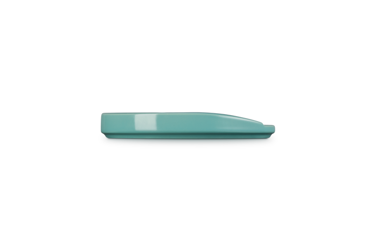 Side view of a blue Riviera Le Creuset oval spoon rest on a black background.