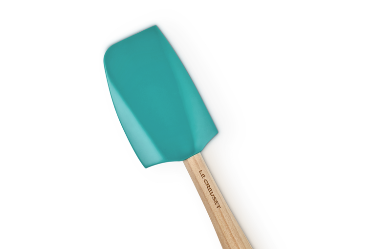 Le Creuset Craft medium spatula with blue silicone head and wooden handle angled on black background.