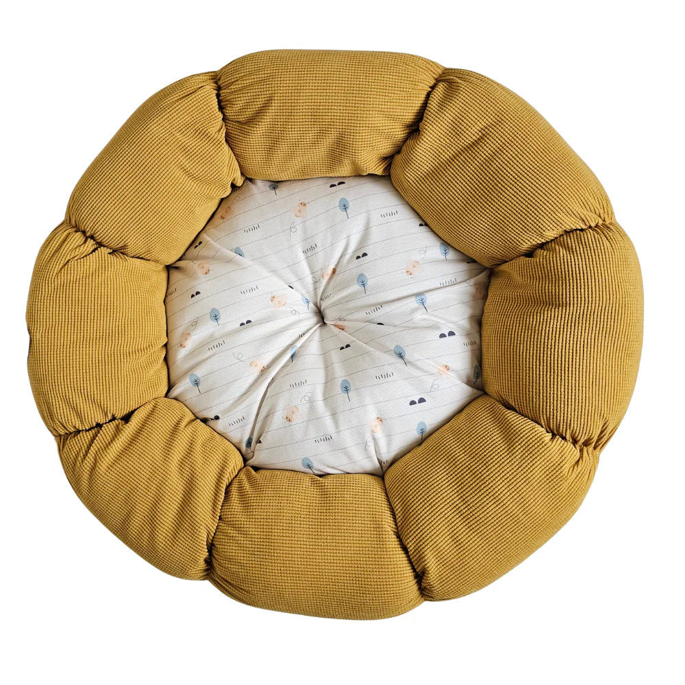 Round pet bed with mustard yellow padded sides and a white cushion featuring small floral and tree prints.