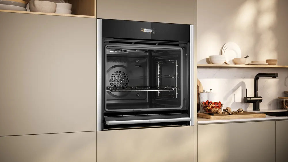 NEFF N70 Slide&Hide electric oven with open door built into beige kitchen cabinetry next to countertop and sink.