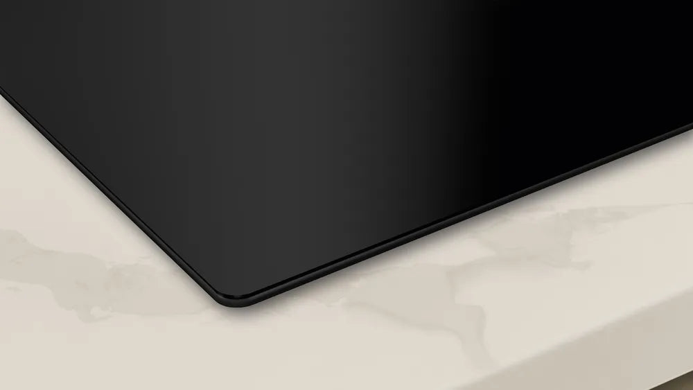 Close-up of the corner of a black Neff N50 induction hob with integrated ventilation on a light marble countertop