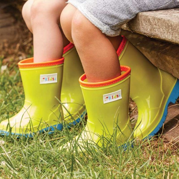 Bright yellow junior wellies with orange trim and blue soles worn by children sitting on grass and wood.