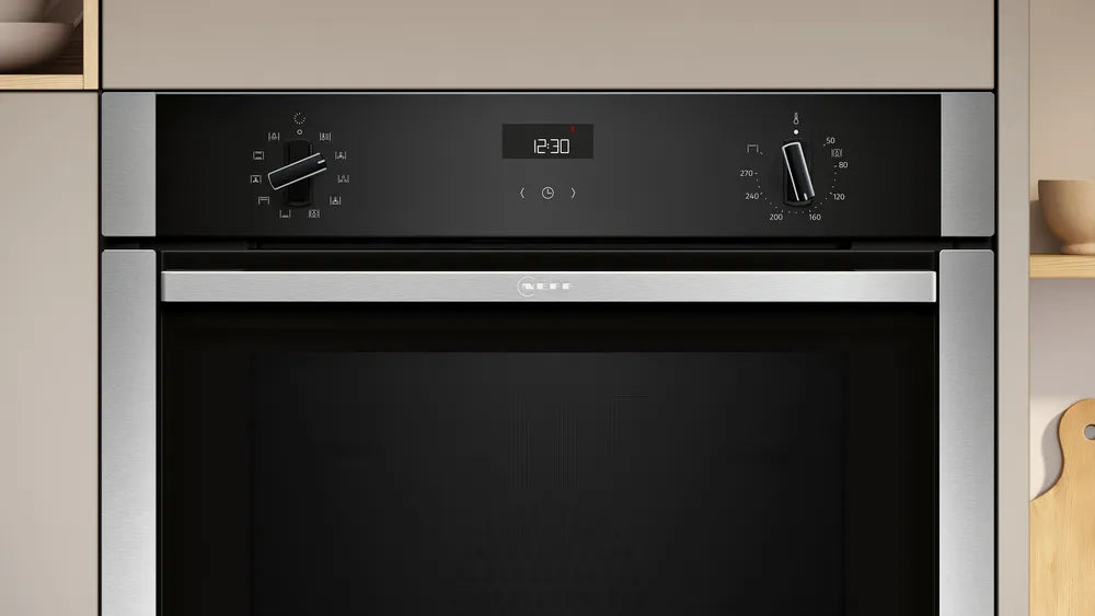 Neff N50 built-in stainless steel oven with black control panel, two knobs, and digital clock showing 12:30.