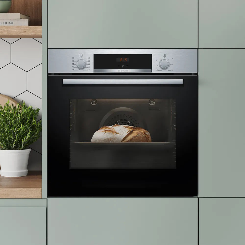 Bosch single oven in stainless steel built into green cabinetry with bread baking inside and digital display on.