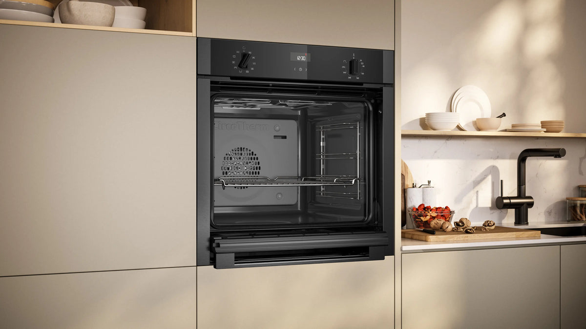 Built-in NEFF N50 Slide & Hide oven in grey with open door, digital display, and control knobs in modern kitchen.