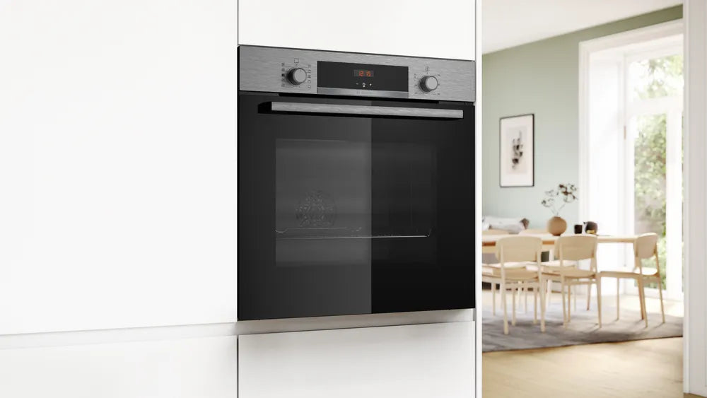 Bosch stainless steel single oven built into white kitchen cabinetry with dining area in background