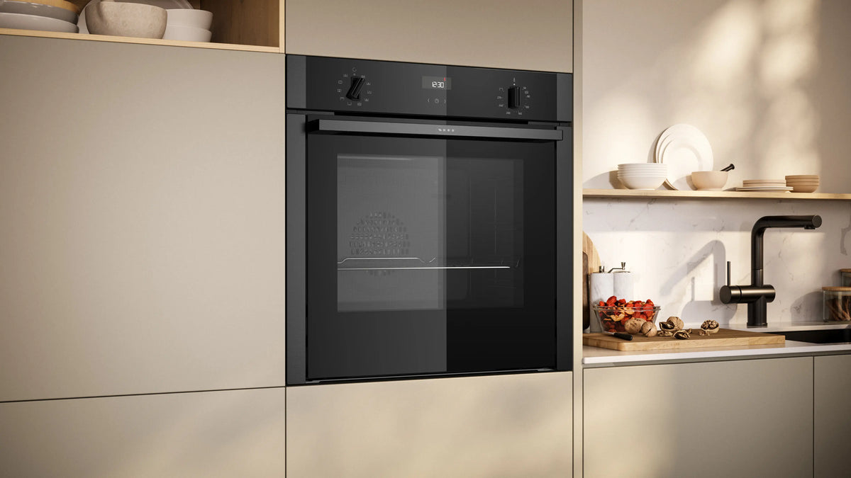 Built-in NEFF N50 Slide & Hide oven in grey integrated into beige kitchen cabinetry next to a sink area.