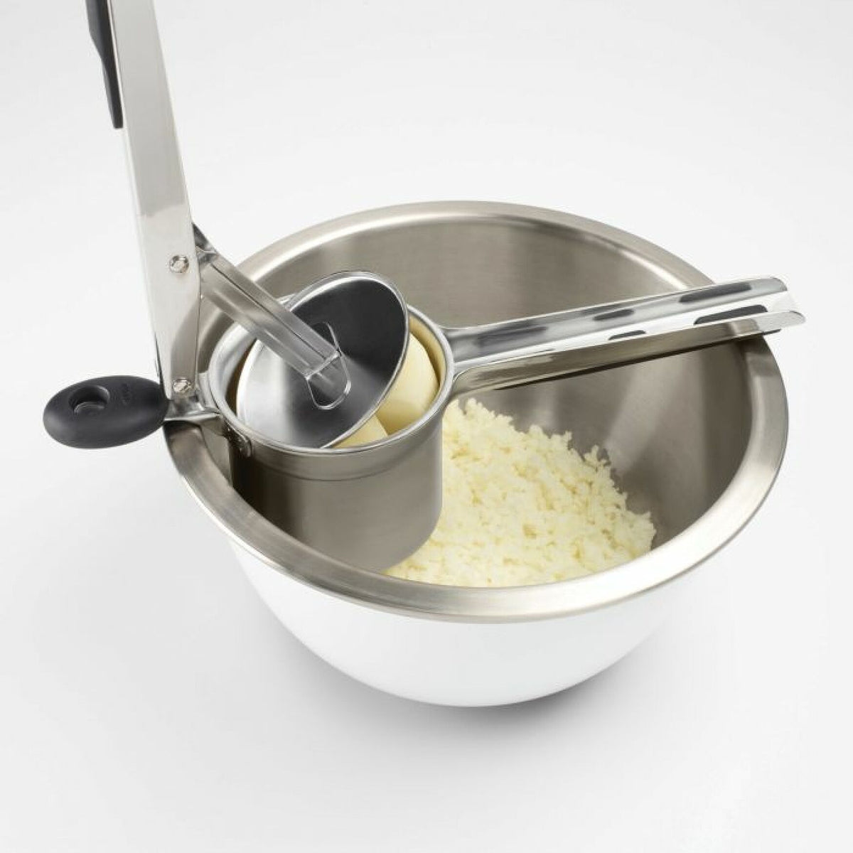Oxo Potato Ricer pressing cooked potato inside a stainless steel bowl with mashed potato visible.