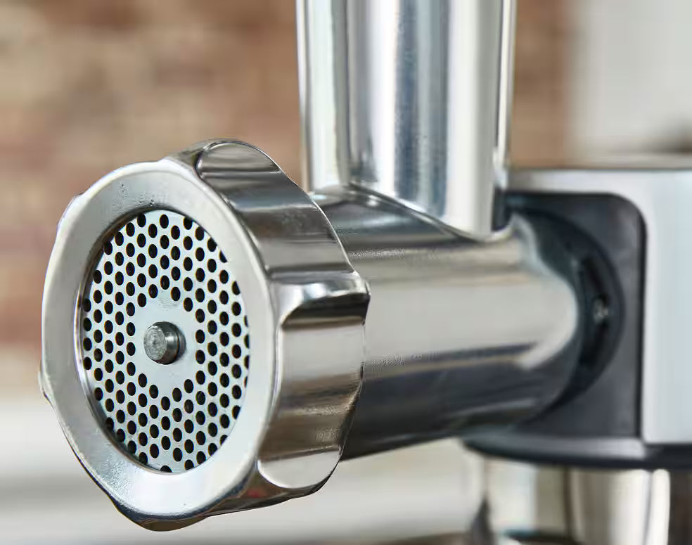 Close-up of the stainless steel Kenwood Meat Grinder Attachment KAX950ME mounted on a kitchen appliance.