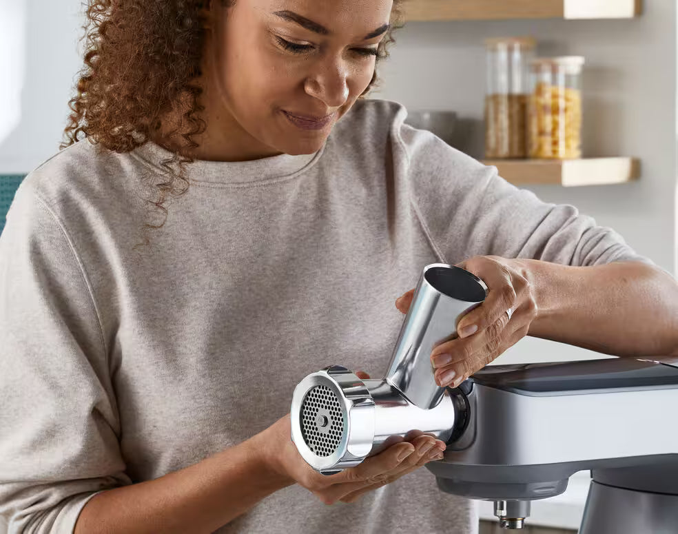 Woman attaching the Kenwood Meat Grinder Attachment KAX950ME to a kitchen mixer in a home kitchen