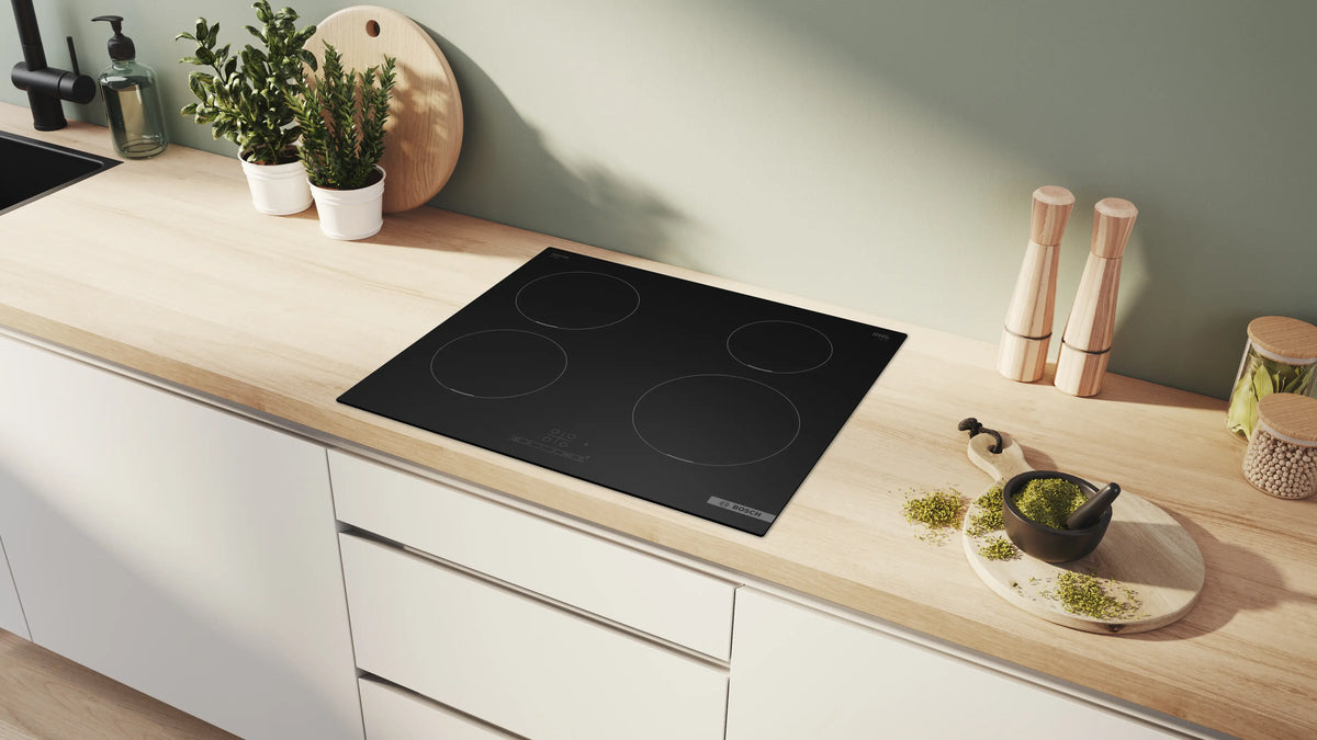 Bosch Series 4 60cm matt black induction hob installed on a light wood kitchen countertop with herbs and wooden utensils