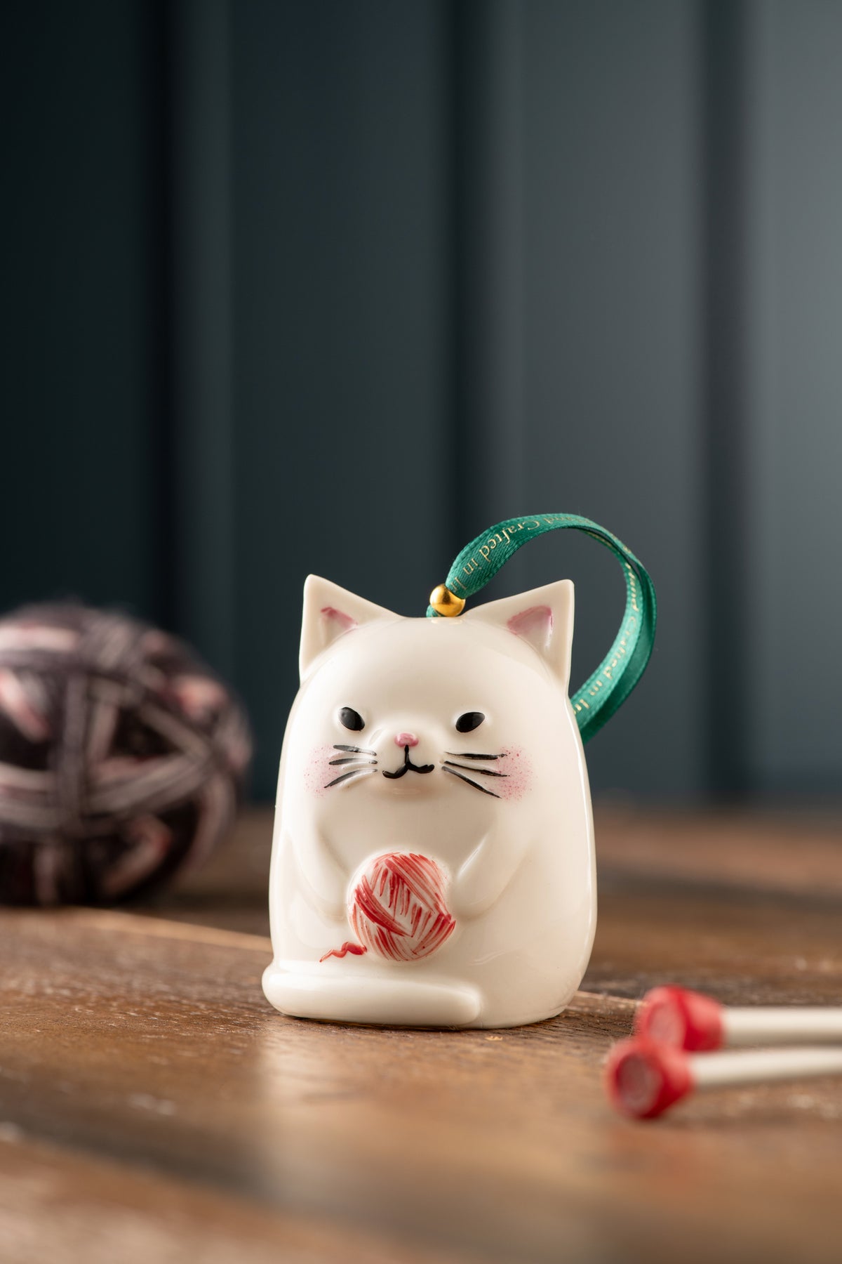 White ceramic Belleek Classic Kitty Cat Ornament holding a red ball of yarn with a green hanging ribbon
