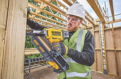 Man wearing safety gear using a DeWalt Twin Nailer Kit 18V to fasten wood framing on a construction site.