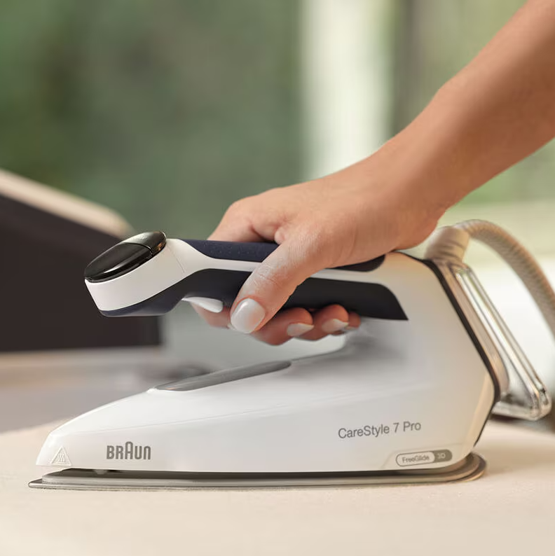 Hand holding Braun CareStyle 7 Pro steam generator iron on a white surface.