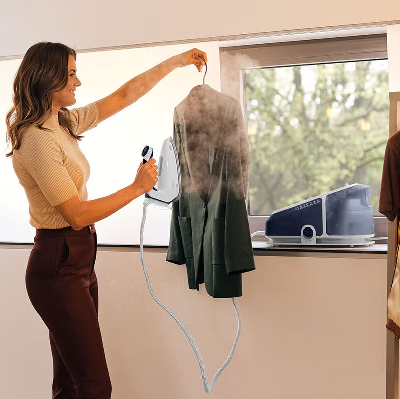 Woman steaming a hanging jacket with Braun Steam Generator Iron near a window.