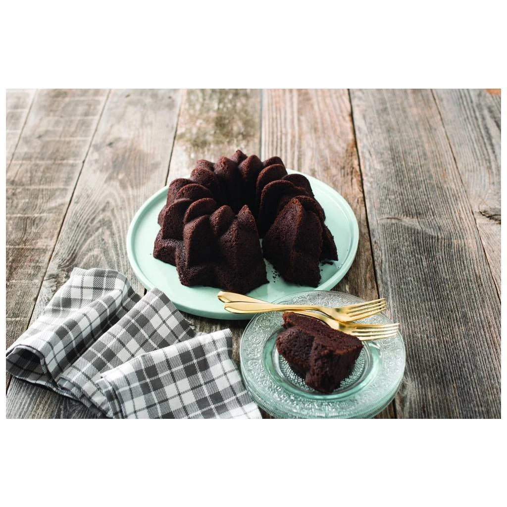 Chocolate bundt cake with star-shaped ridges on a light blue plate, slice served on a glass plate with gold forks.