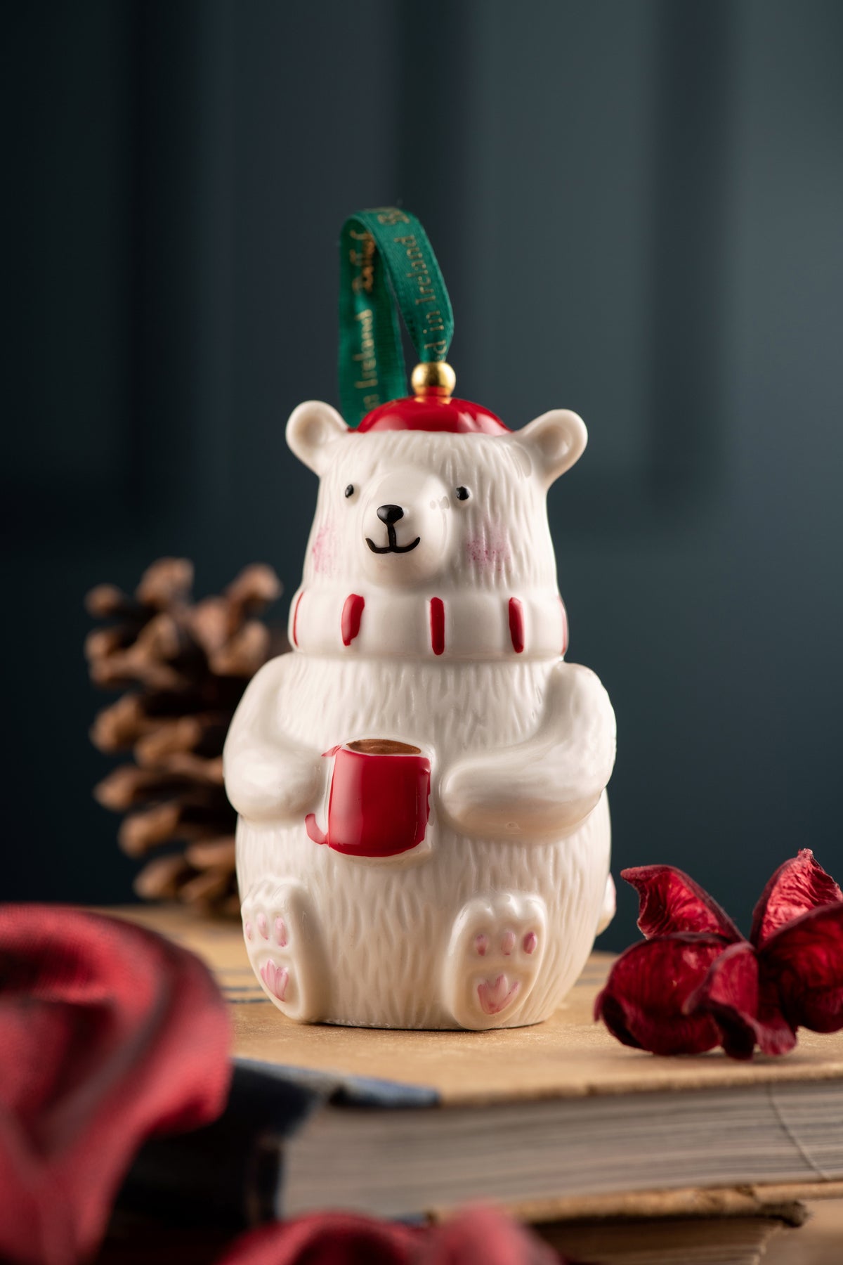 Belleek Classic Polar Bear Ornament holding a red mug, wearing a red hat and scarf, with a green hanging ribbon.