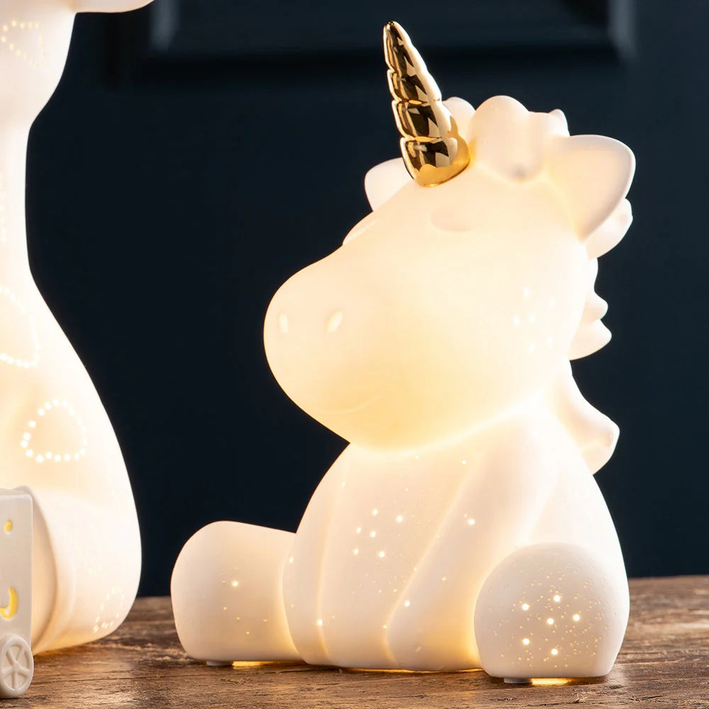 Unicorn Luminaire glowing softly with a golden horn, sitting on a wooden surface against a dark background.
