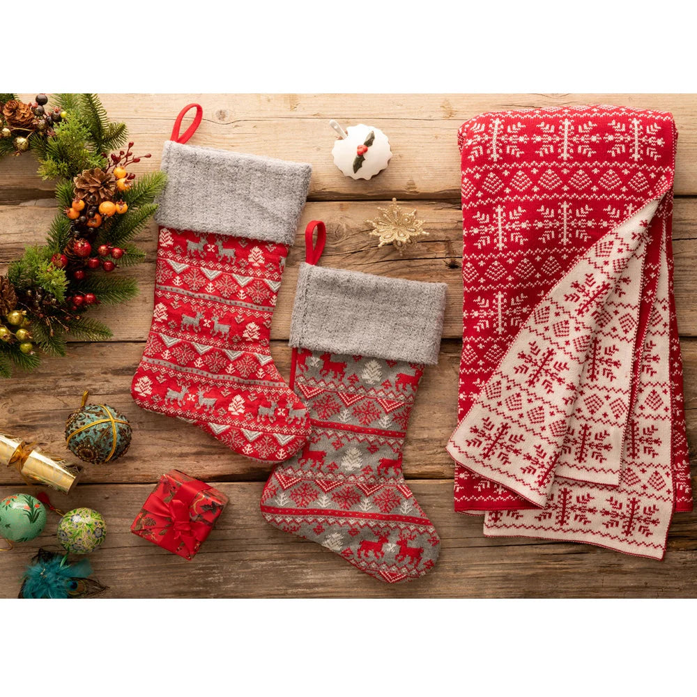 Two Christmas red Fairisle stockings with grey cuffs, surrounded by holiday decorations on a wooden surface.