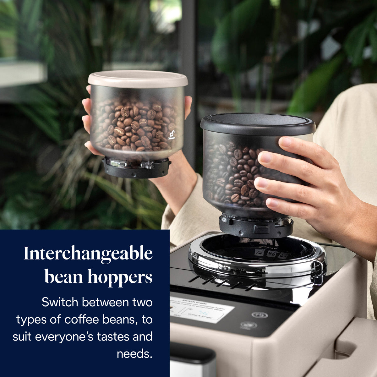 Hands holding two interchangeable coffee bean hoppers filled with beans above the DeLonghi Rivelia coffee machine.