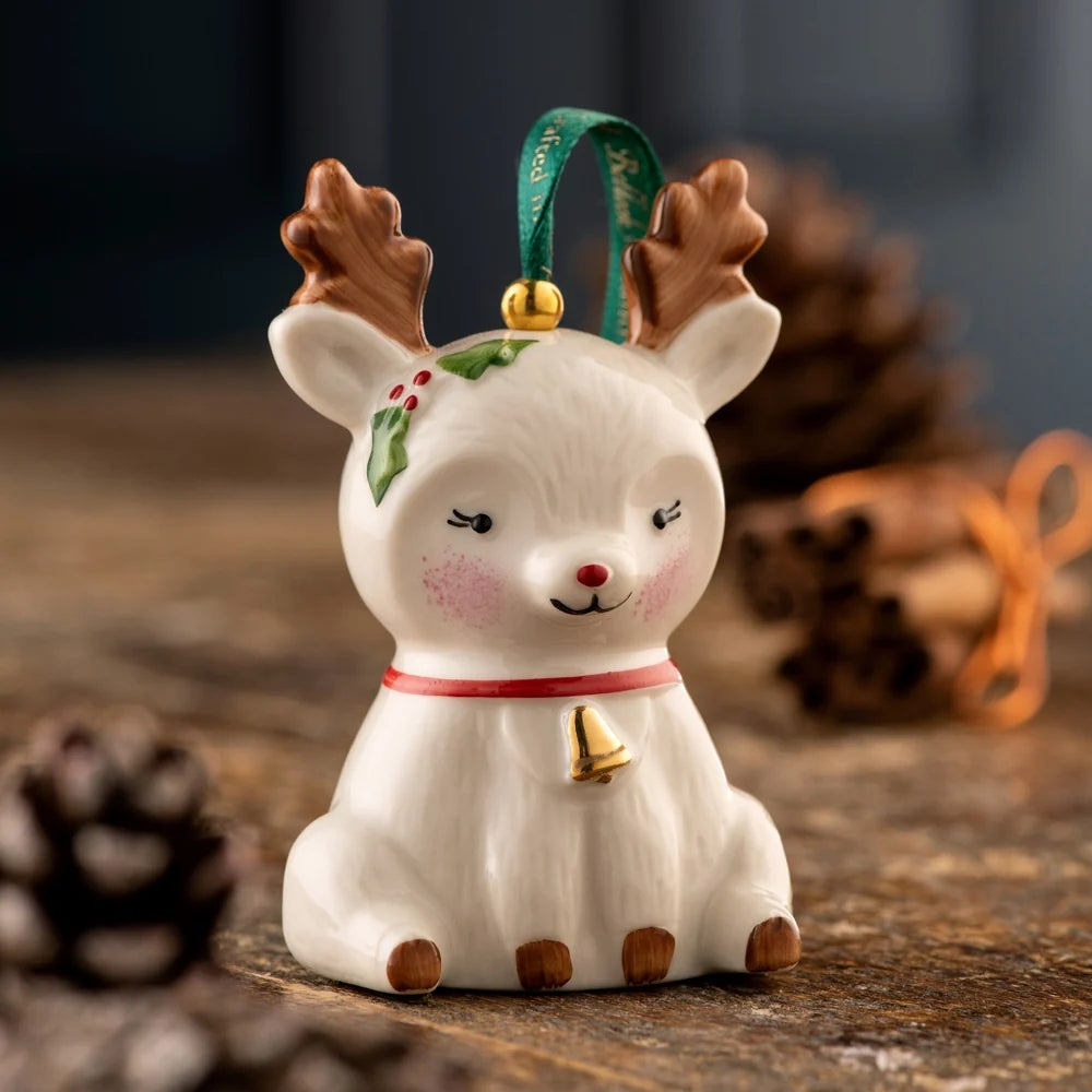 White ceramic Belleek reindeer ornament with brown antlers, red nose, holly detail, and gold bell collar.
