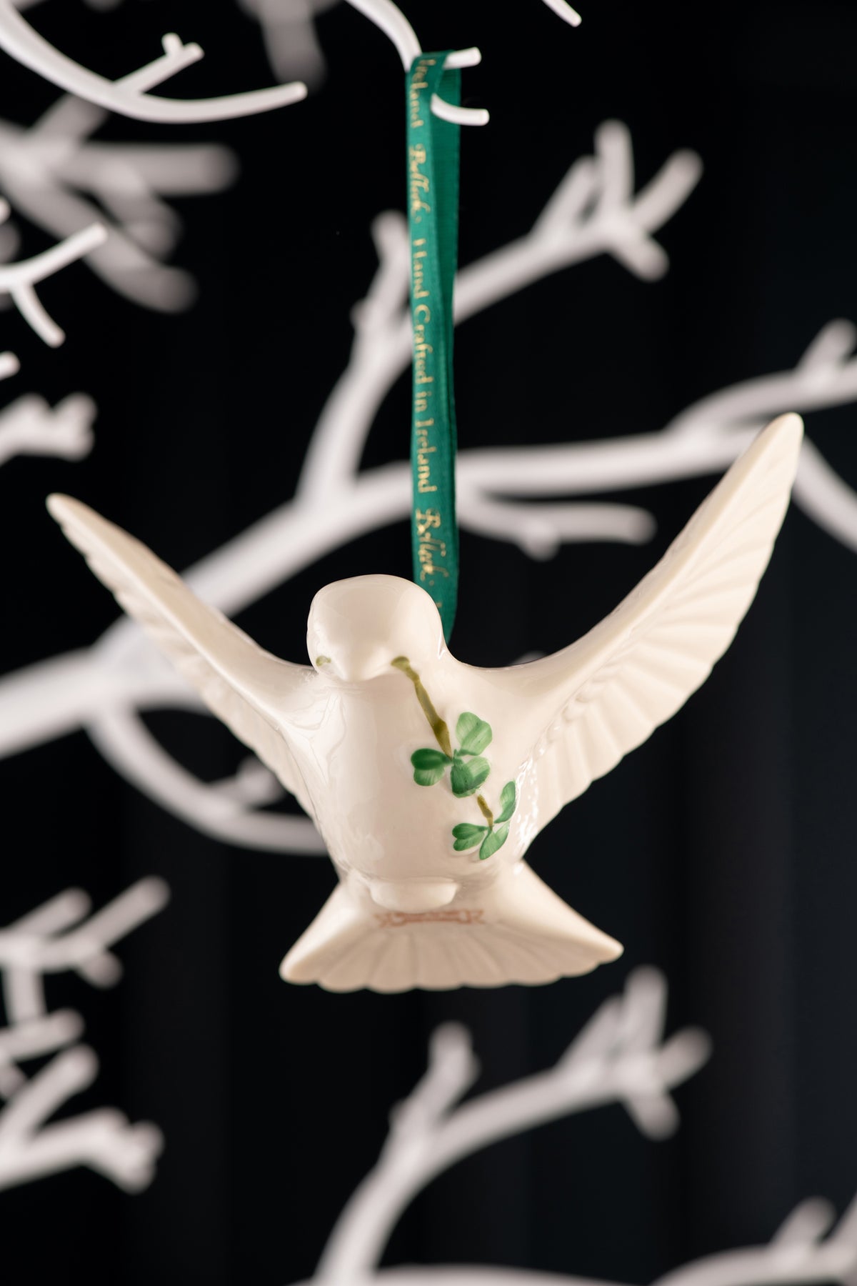 Belleek Classic Dove Ornament hanging from green ribbon with white decorative branches in background