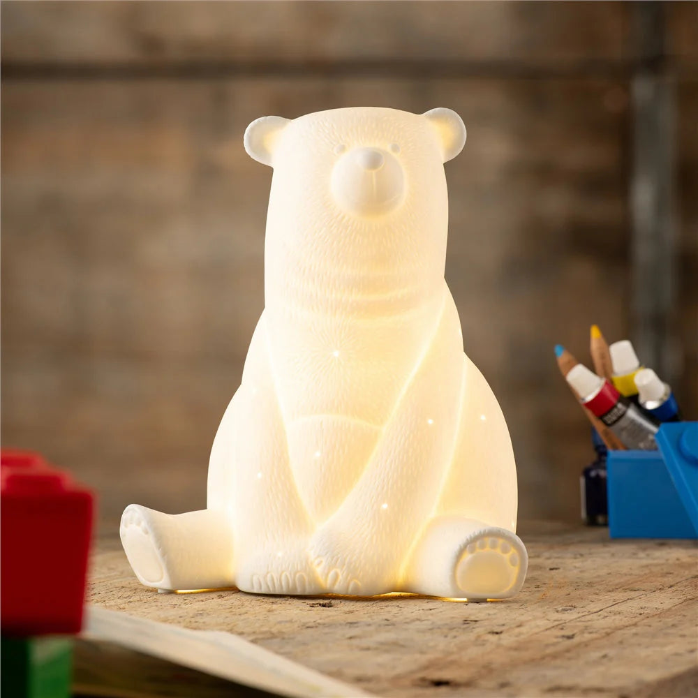 Lit Luminaire Polar Bear LED lamp sitting on a wooden surface with art supplies nearby.