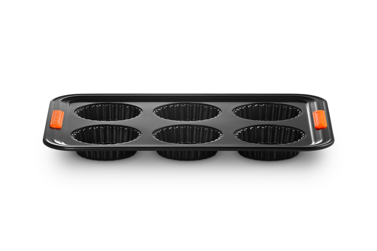 Le Creuset 6 cup tart tray with non-stick black surface and orange silicone grips on each end.