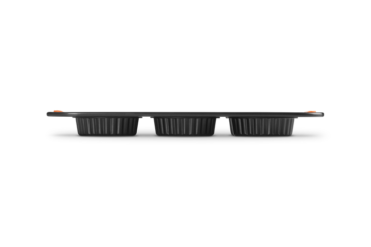 Side view of Le Creuset 6 cup tart tray in black with fluted edges and orange handles.