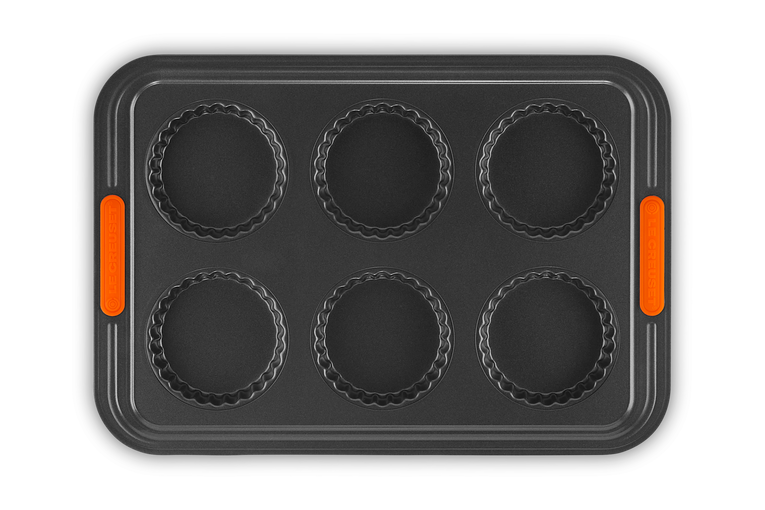 Le Creuset 6 cup tart tray with non-stick fluted tart molds and orange silicone handles.