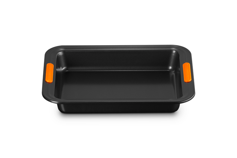 Le Creuset 28cm rectangular black bakeware tin with orange silicone grip handles, front view.