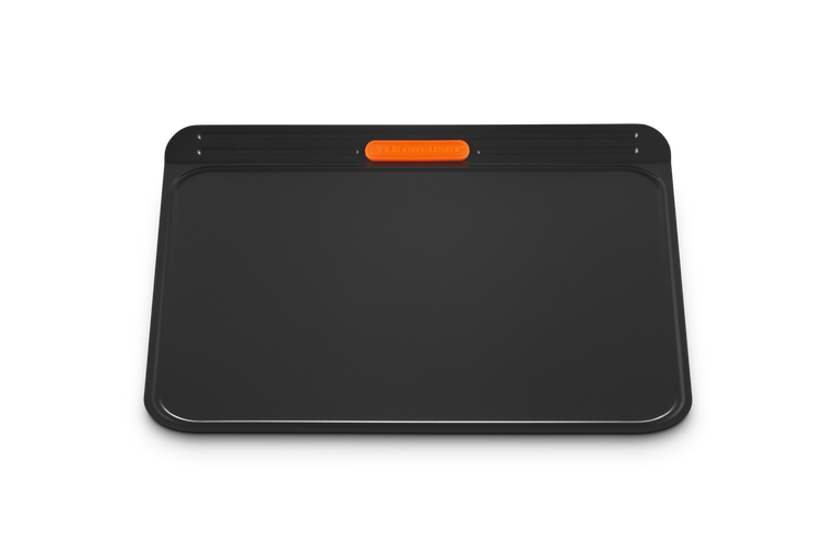 Le Creuset insulated cookie sheet in black with an orange silicone grip on the top edge.