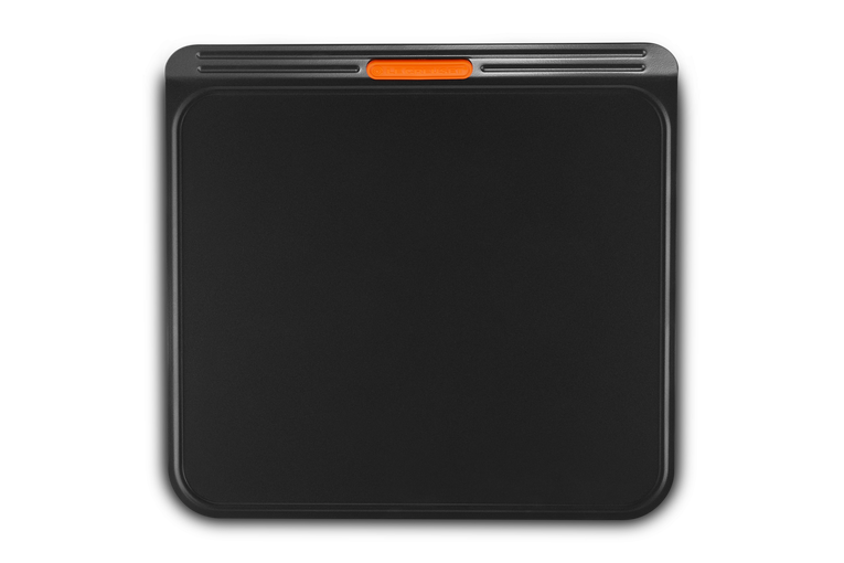 Le Creuset insulated non-stick cookie sheet with flat edges and orange silicone grip handle, top view.