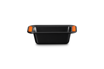 Le Creuset black non-stick 1LB loaf tin with orange silicone grip handles, shown from the side.