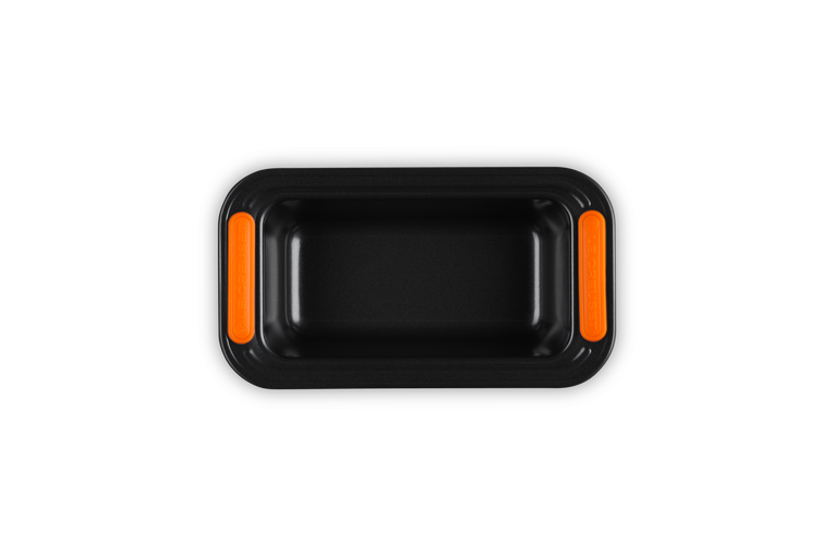 Le Creuset black non-stick 1LB loaf tin with orange silicone grip handles, top view on black background
