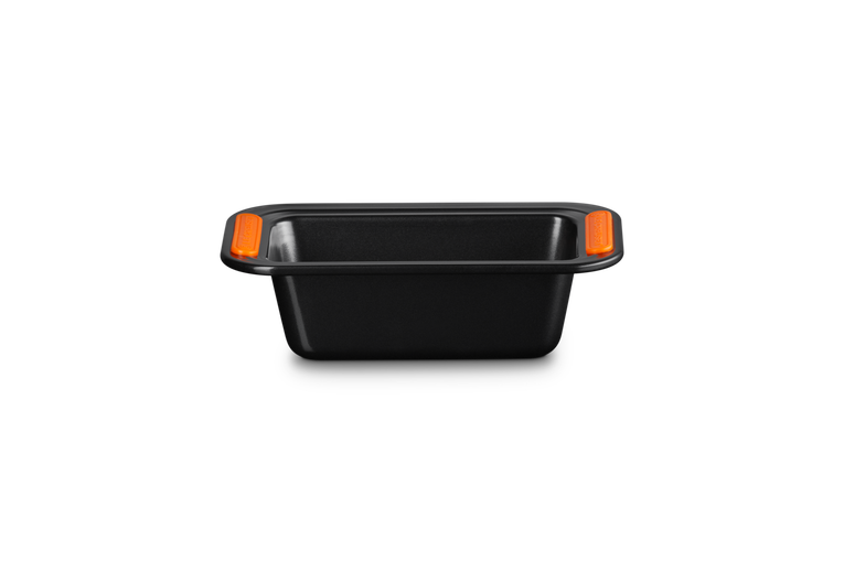 Le Creuset rectangular loaf tin with non-stick black surface and orange heat-resistant silicone handles.