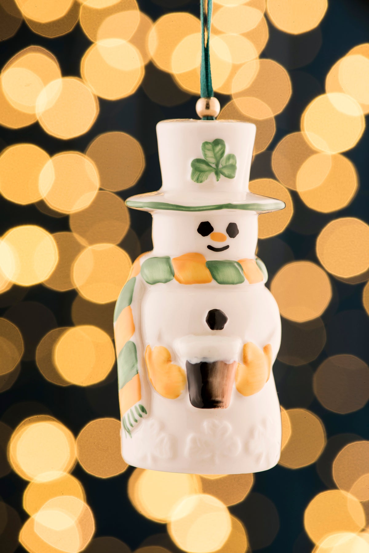 Belleek Paddy Snowman Ornament with green shamrock hat and orange-green scarf against blurred lights background