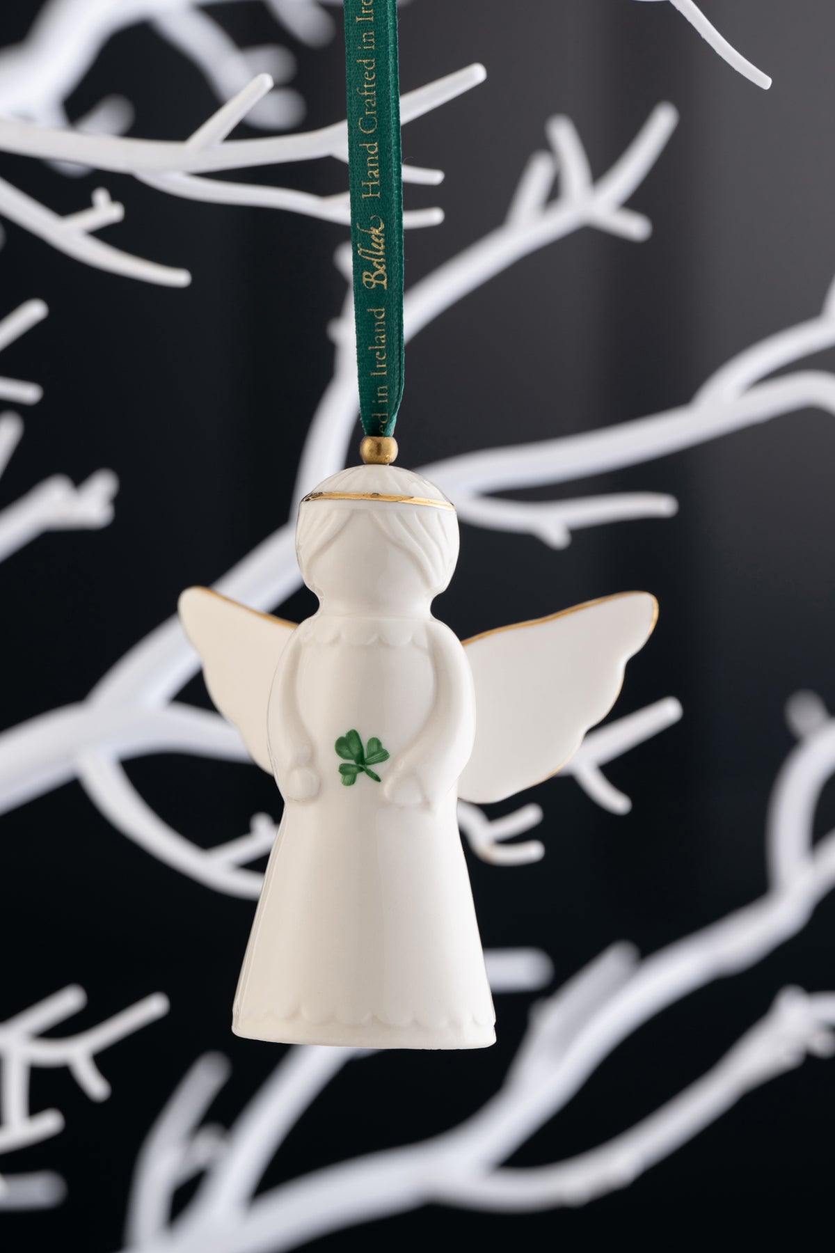 Belleek Classic Irish Angel Ornament with gold trim and green shamrock, hanging on a green ribbon against white branches.