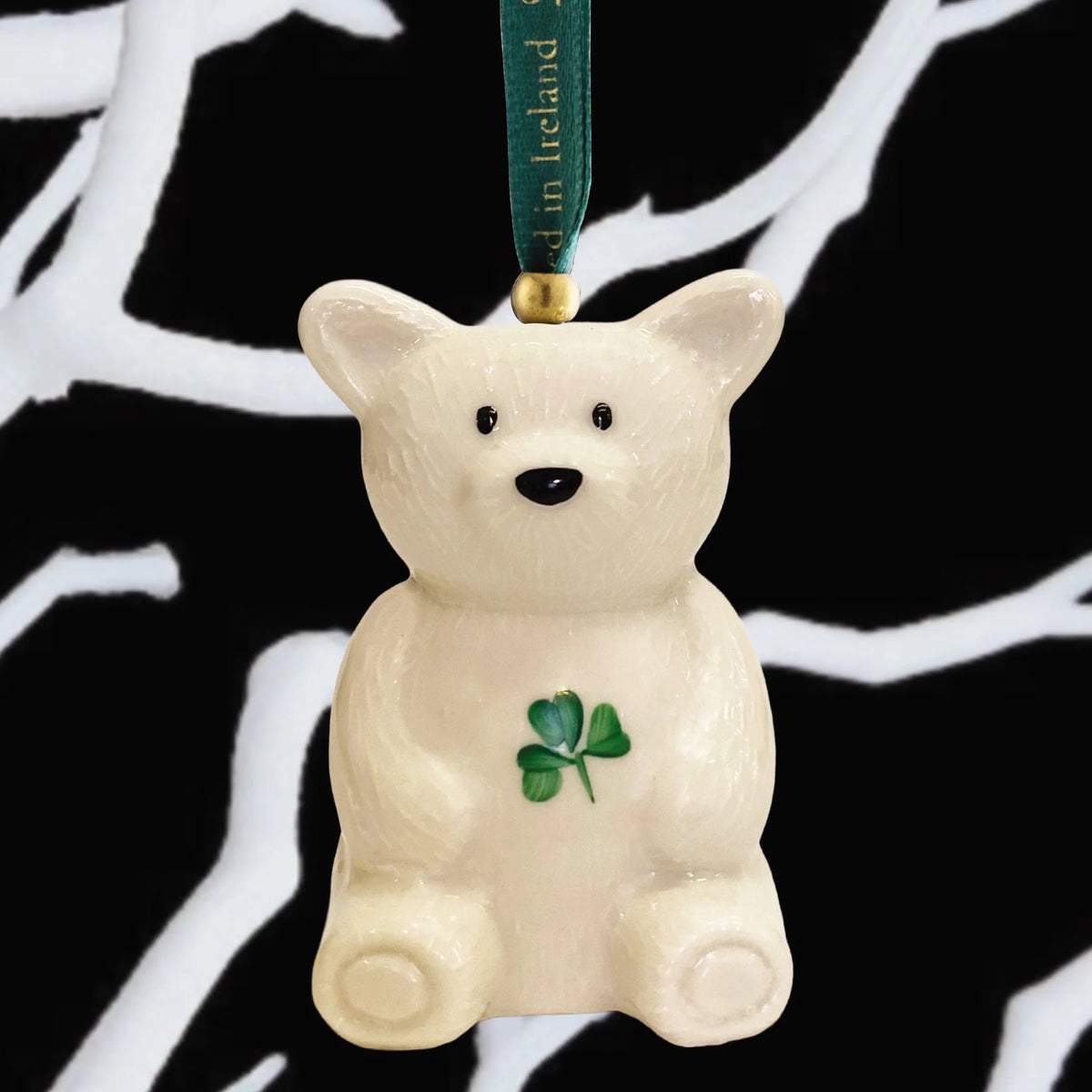 Cream-colored Belleek Teddy Ornament holding a green shamrock with a green hanging ribbon.