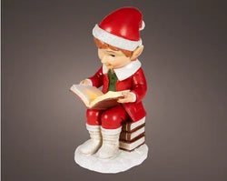Christmas elf figurine reading a book on a gray background