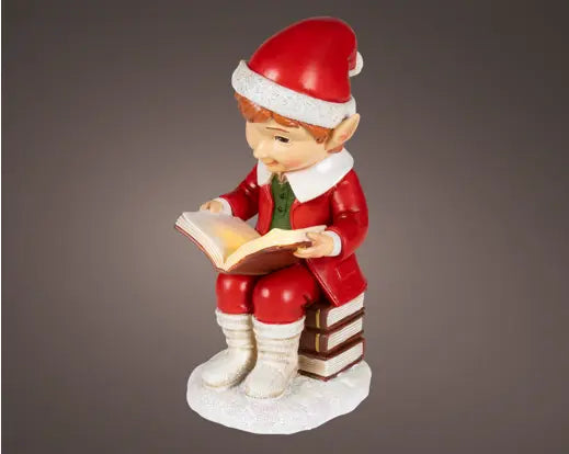 Christmas elf figurine reading a book on a gray background